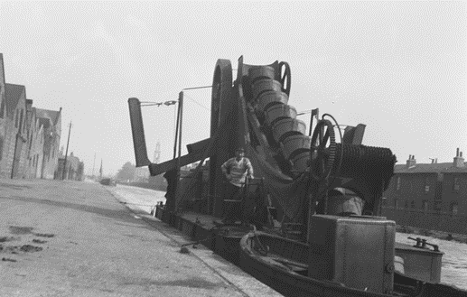 Surrey Canal, the bucket dredger 'Surrey' lies alongside a wharf near the Camberwell basin, c1930. St Georges Church, Wells Way, in the background.  X ..png