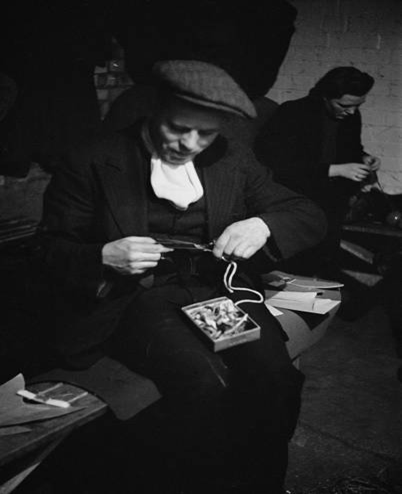 Mr Rendle cuts out the soles of a pair of slippers at a craft lesson given by LCC teachers in a air raid shelter during the Blitz 1941.  X..png