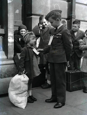 World War Two, London, 10th, September 1942. Young child Brian Lee wearing his RAF uniform, studies the evacuation label on a model evacuee, Alice King aged 5, from Rotherhithe.    X..png