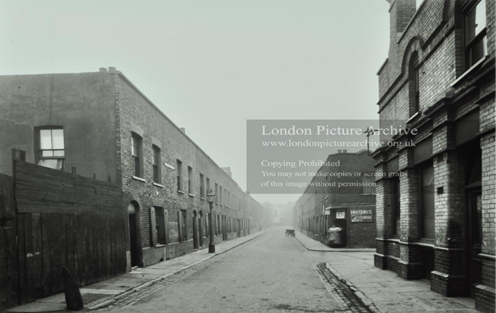 Camelot Street in Tabard Estate, the corner shop advertising R. Whites American cream soda and lemonade, coal at 1s5d. A delivery bicycle is parked in the street, c1913. 1  X..png