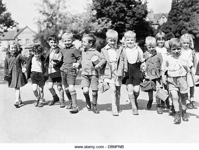 A group of smiling evacuees from Rotherhithe, with gas mask boxes hold hands on a walk in Reading  c1940..jpg