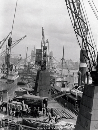 Workers loading and unloading on a busy London dock, c 1930s..png